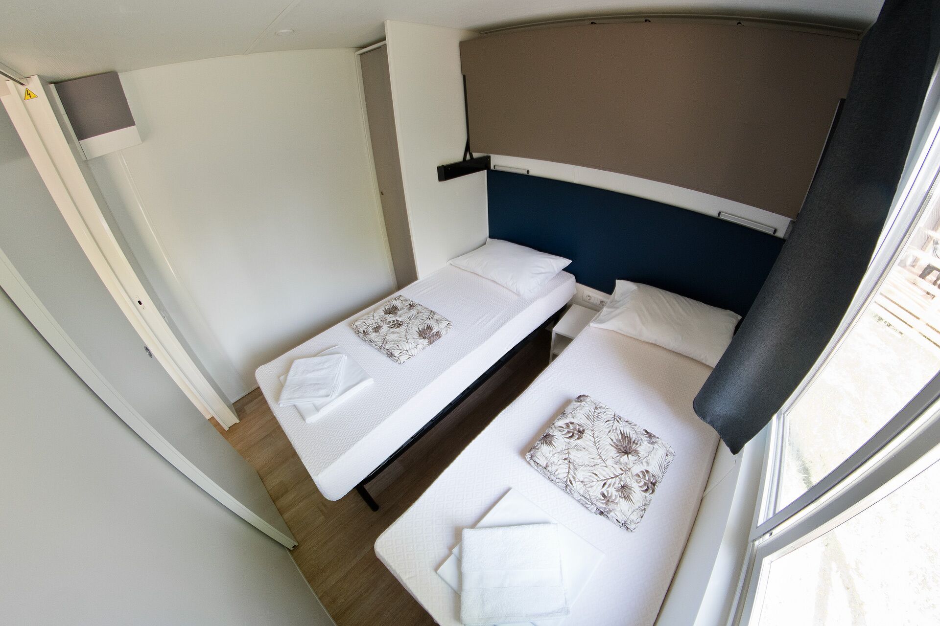 Een kleine kamer met twee bedden, een raam en een deur.