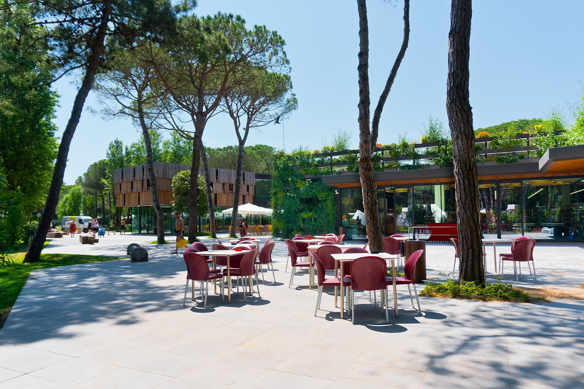 An outdoor cafe area with tables and chairs, surrounded by trees and a building with a modern design.