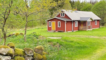 Una casa de madera roja con un porche, rodeada de césped verde y árboles.