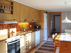 Una cocina con armarios de madera, horno empotrado, un lavabo y una zona de comedor con mesa y sillas.