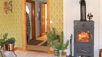 Una habitación con puerta de madera, una chimenea encendida y dos plantas en macetas.