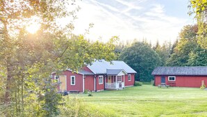 A red building with a porch, surrounded by a grassy field and trees. - 4 Star Holiday Home in Ullared (Ullared)