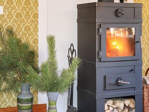 A wood-burning stove with a glass door, a vase with pine branches, and a pair of scissors on a table. - 4 Star Holiday Home in Ullared (Ullared)