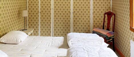 Una habitación con dos camas, una mesita, una silla y papel tapiz estampado.