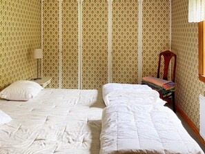Una habitación con dos camas, una mesita, una silla y papel tapiz estampado.