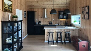 A wooden-paneled kitchen with a central island, black bar stools, and a red chest of drawers. - 4 Star Holiday Home in Skare (Ullensvang)