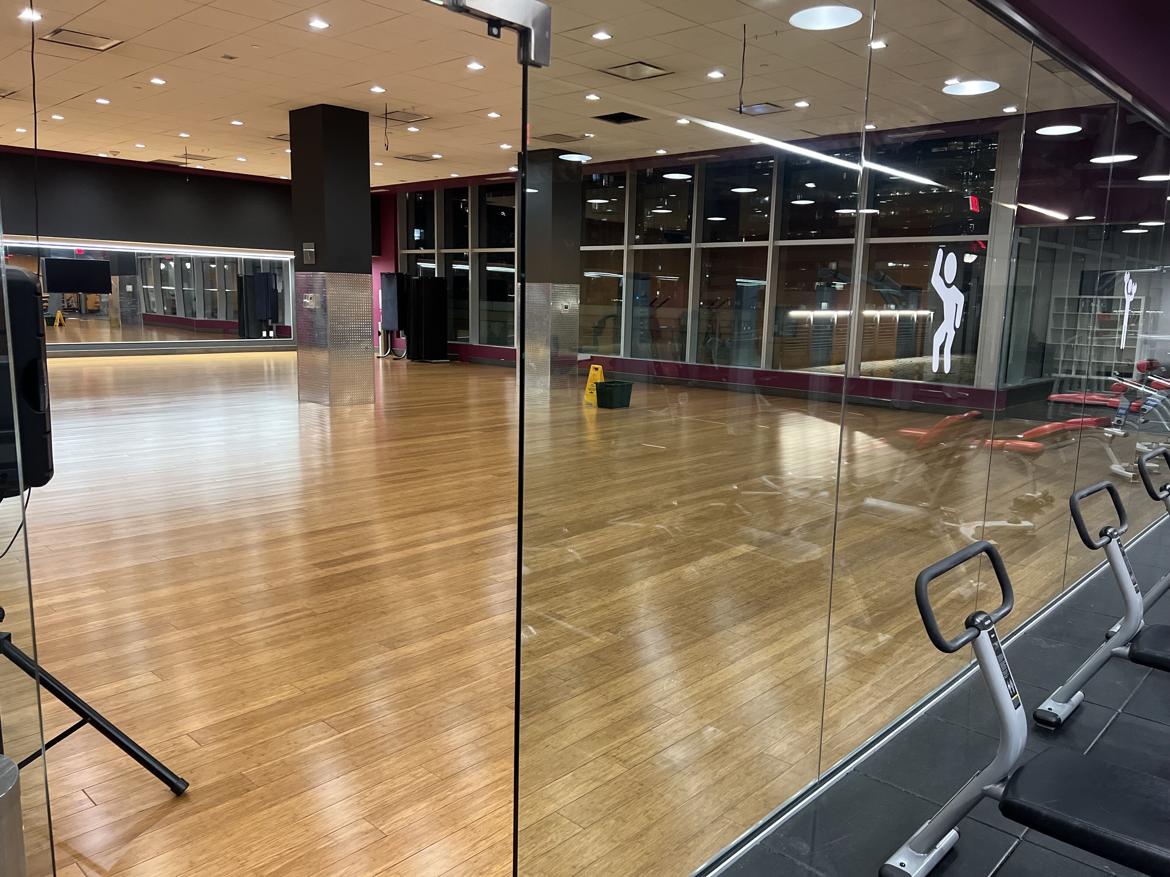 A gym with wooden floors, exercise equipment, and large windows.