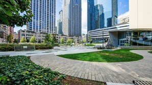 Una plaza urbana moderna con un sendero pavimentado, áreas verdes y edificios altos al fondo.