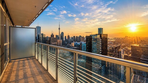 Un balcón con vista al horizonte de la ciudad, incluyendo una torre destacada, durante el atardecer.