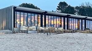 A modern building with large glass windows, outdoor seating, and a sandy ground. - 4 Star Holiday Home in Gotlands Tofta (Gotlands Tofta)