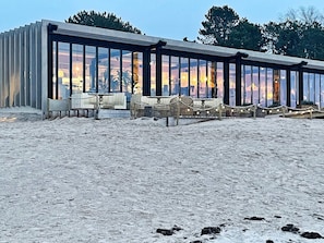 A modern building with large glass windows, outdoor seating, and a sandy ground. - 4 Star Holiday Home in Gotlands Tofta (Gotlands Tofta)