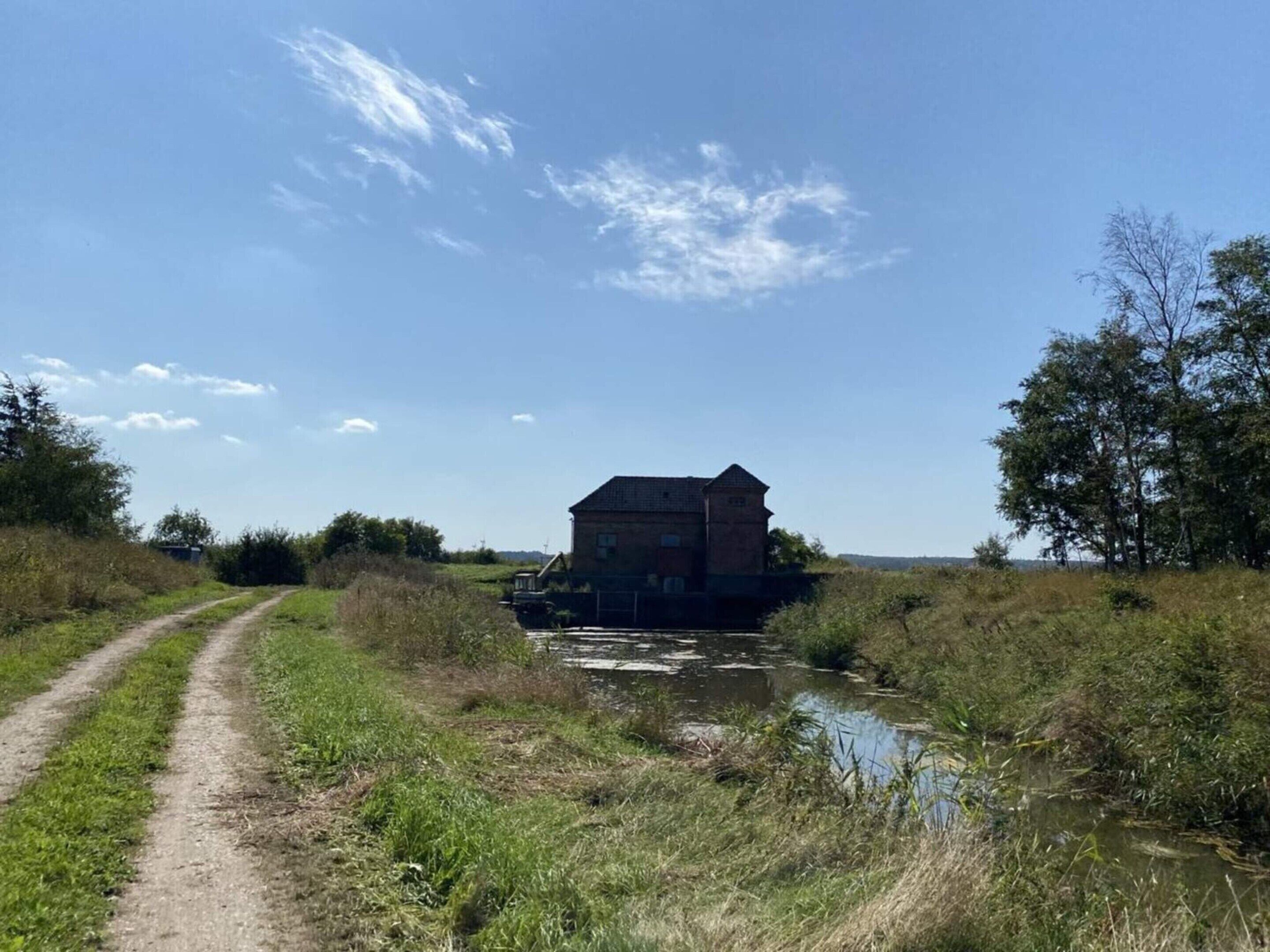 A rural setting with a dirt path leading to a brick building by a water body.