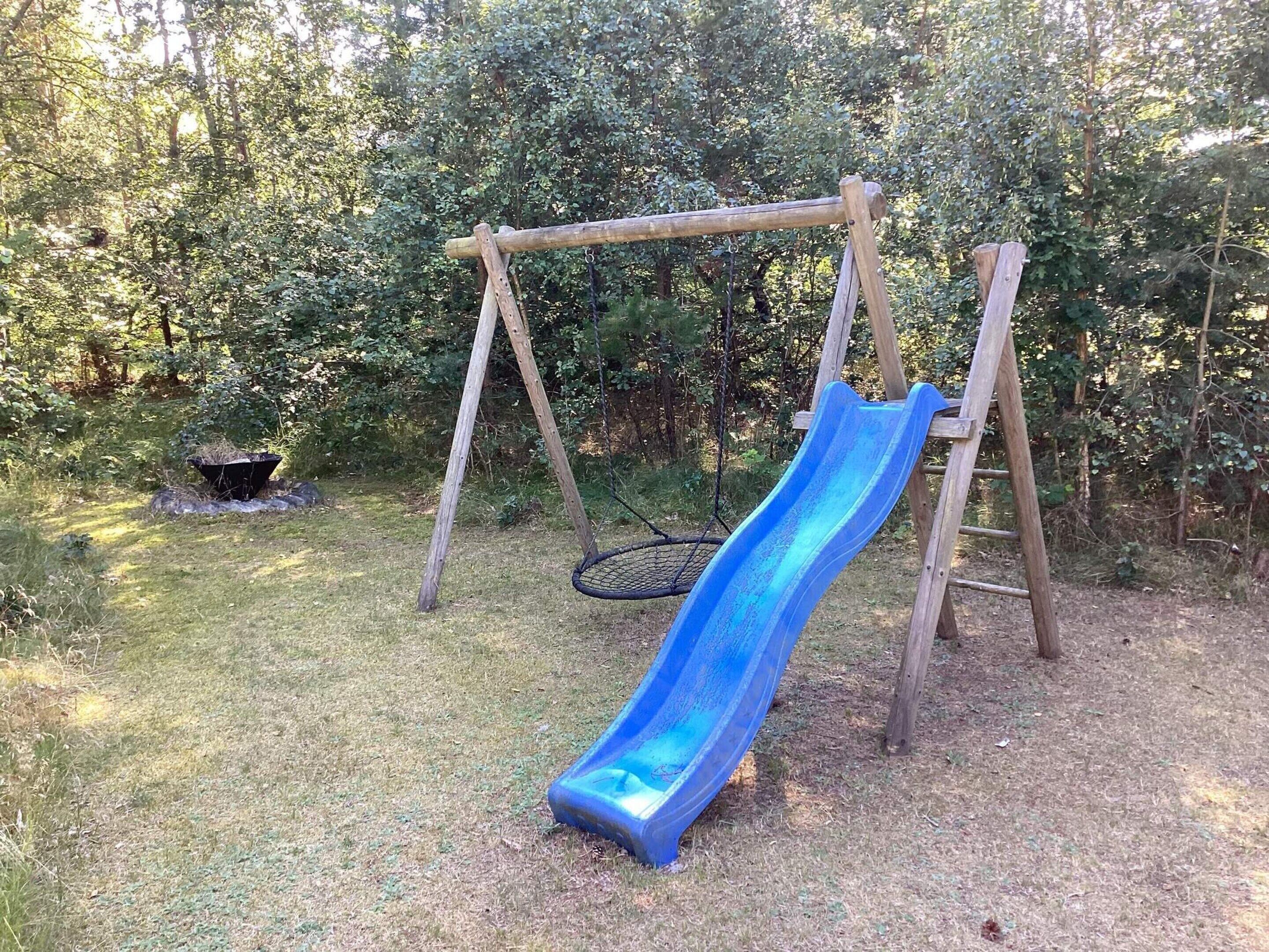 Un ensemble de jeux d’extérieur en bois, avec un toboggan bleu, installé dans une cour arrière verdoyante et entouré d’arbres.