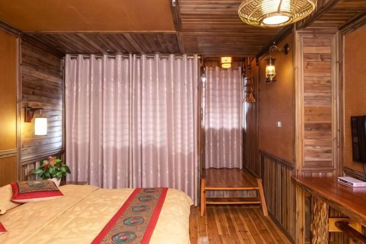 A room with a bed, a wooden bench, a TV, and a wall-mounted light fixture.