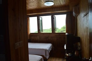 A wooden cabin room with two beds, a coffee machine, and a large window offering a view of greenery.