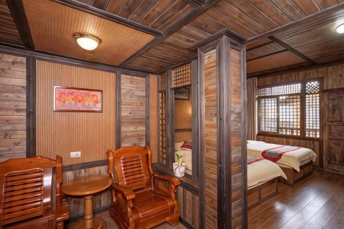 A room with wooden walls and ceiling, a bed with a red and white bedspread, a wooden chair, and a small table.