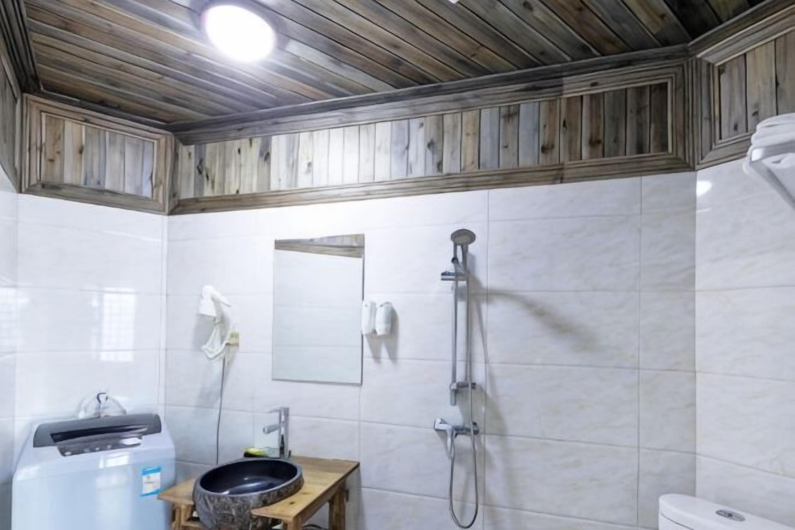 A bathroom with a wooden ceiling, white tiles, a mirror, a sink, and a shower.