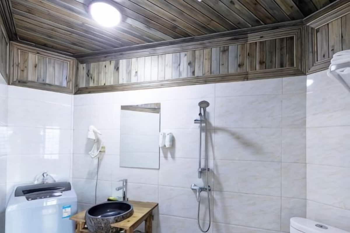 A bathroom with a wooden ceiling, white tiles, a mirror, a sink, and a shower.