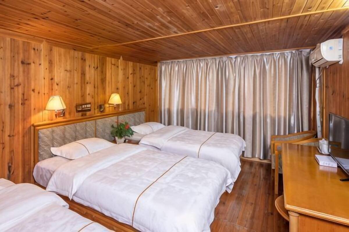 A room with four beds, wooden walls, a wooden desk, and a window with curtains.
