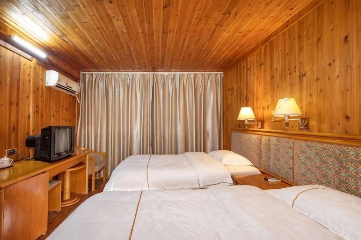 A wooden-paneled room with two beds, a desk with a television, and two wall-mounted lamps.