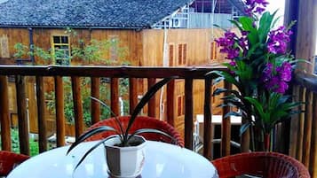 A wooden deck with a table and chairs, a potted plant, and a view of a building in the background.