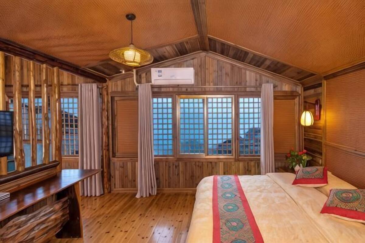 A wooden cabin-style room with a bed, a television, and a large window with curtains.