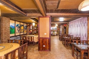 Interior de restaurante con mesas y sillas de madera, un pilar central y obras de arte enmarcadas en las paredes.