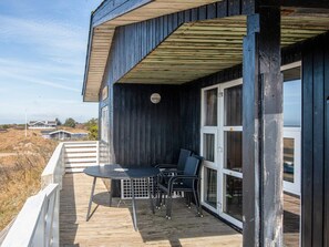 A wooden deck with a table and chairs, a covered area with a window, and a view of the landscape. - 6 Person Holiday Home in Fano (Fano)