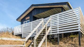 A building with a wooden staircase leading to a covered area, a sign reading 'Kikkeberg,' and a clear sky.