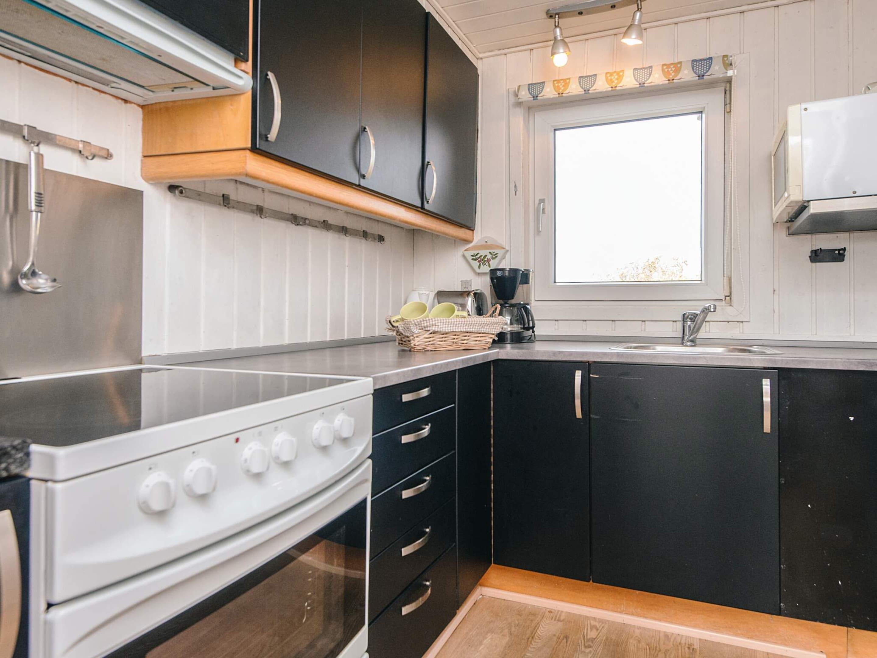 Una cocina compacta con estufa, horno, gabinetes negros y un ventanal.