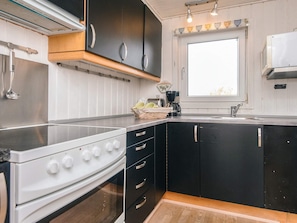 A compact kitchen with a stove, oven, black cabinets, and a window. - 6 Person Holiday Home in Fano (Fano)