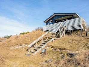 A wooden staircase leading to a blue building with a sloped roof, situated on a grassy hill.