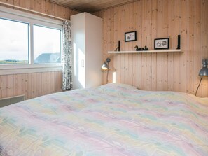 A bedroom with a large bed, a window, wooden walls, a white wardrobe, and a shelf with decorative items. - 6 Person Holiday Home in Fano (Fano)