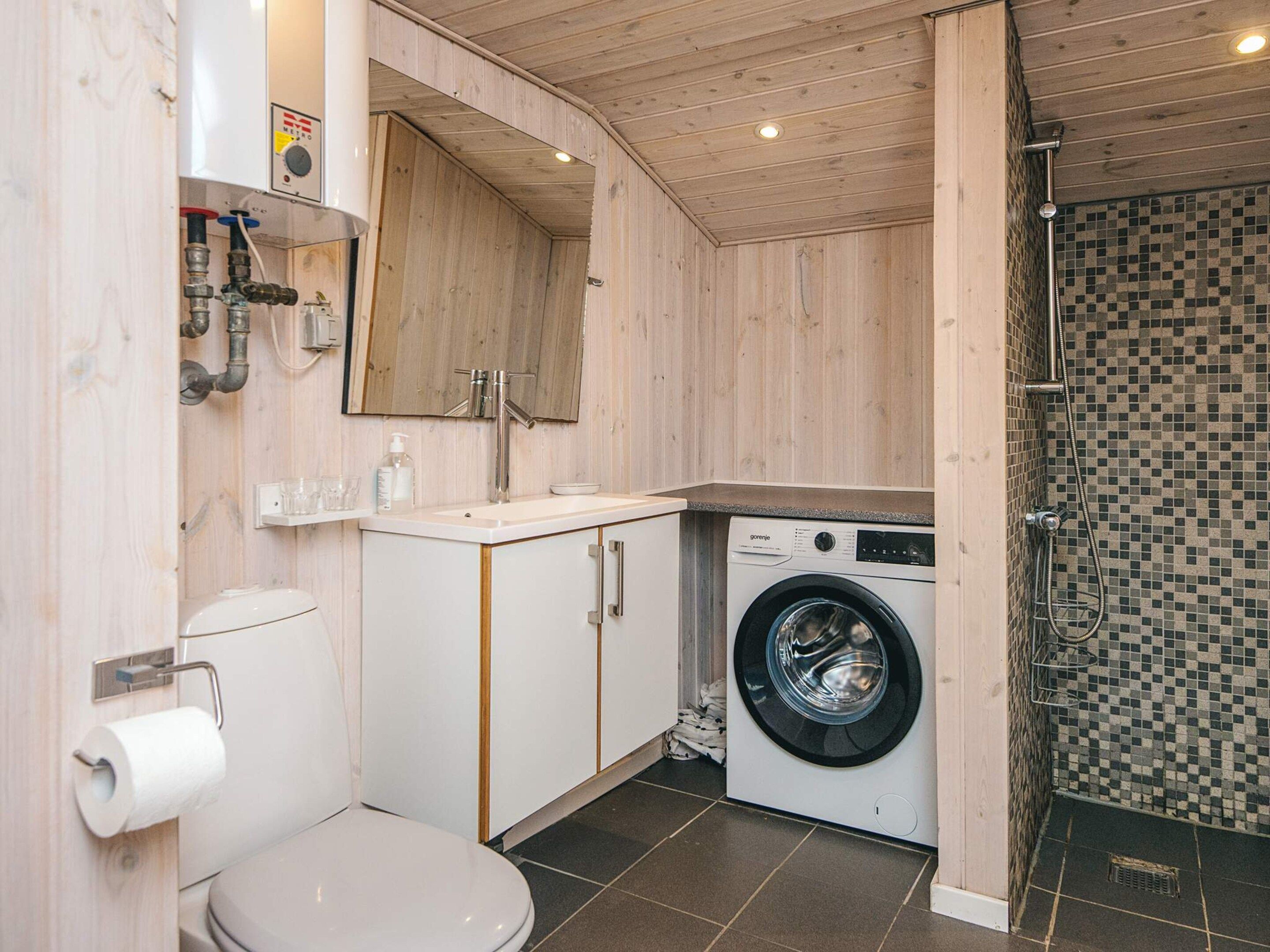 Ein kleines Badezimmer mit Toilette, Waschbecken, Spiegel, Waschmaschine und Duschbereich.