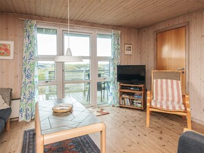 A cozy living room with a wooden floor, a television on a wooden stand, a striped armchair, and a dining table with a rug.