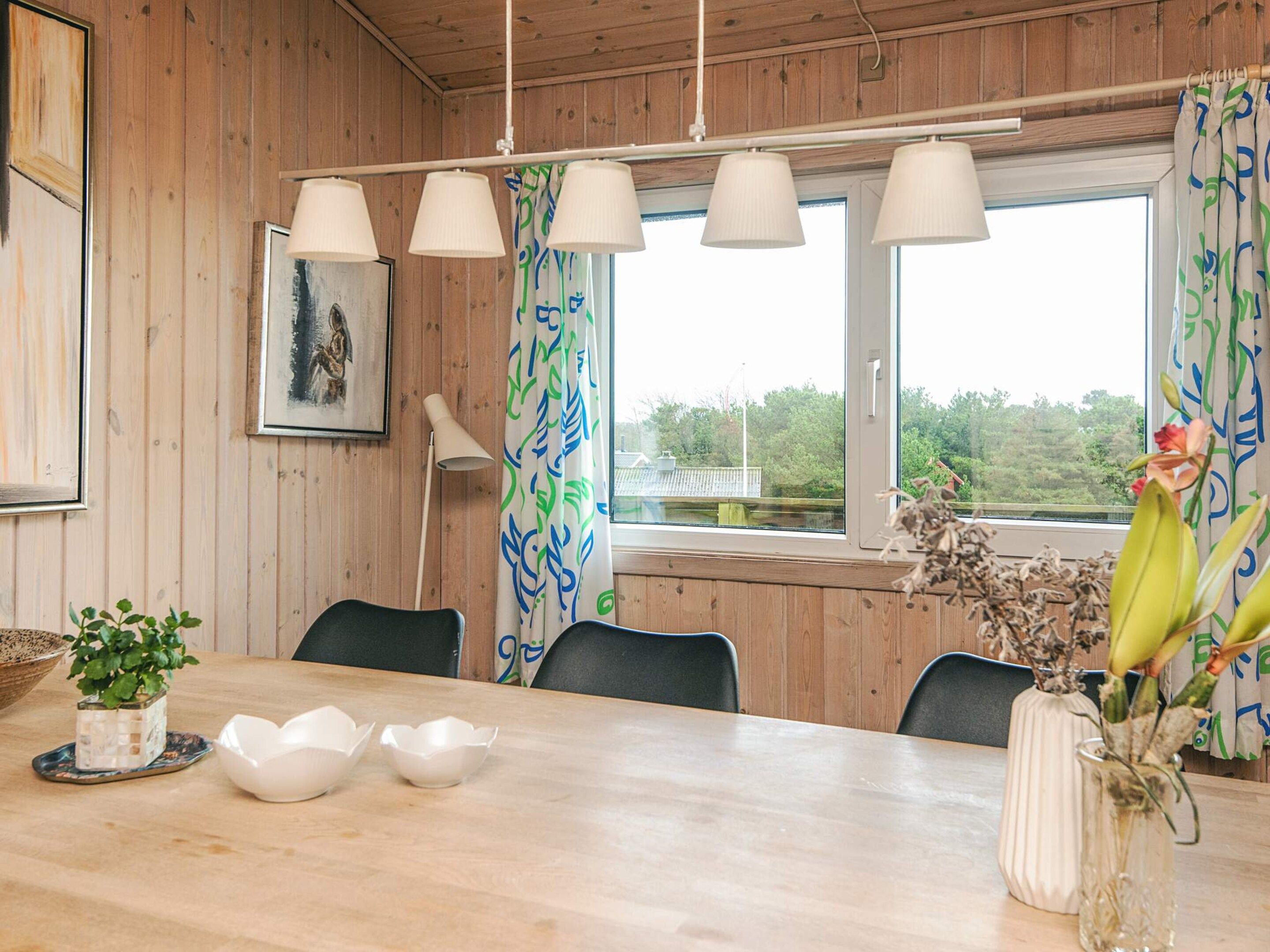 Un intérieur en bois comprenant une table à manger, des chaises, une lampe et une fenêtre avec des rideaux.