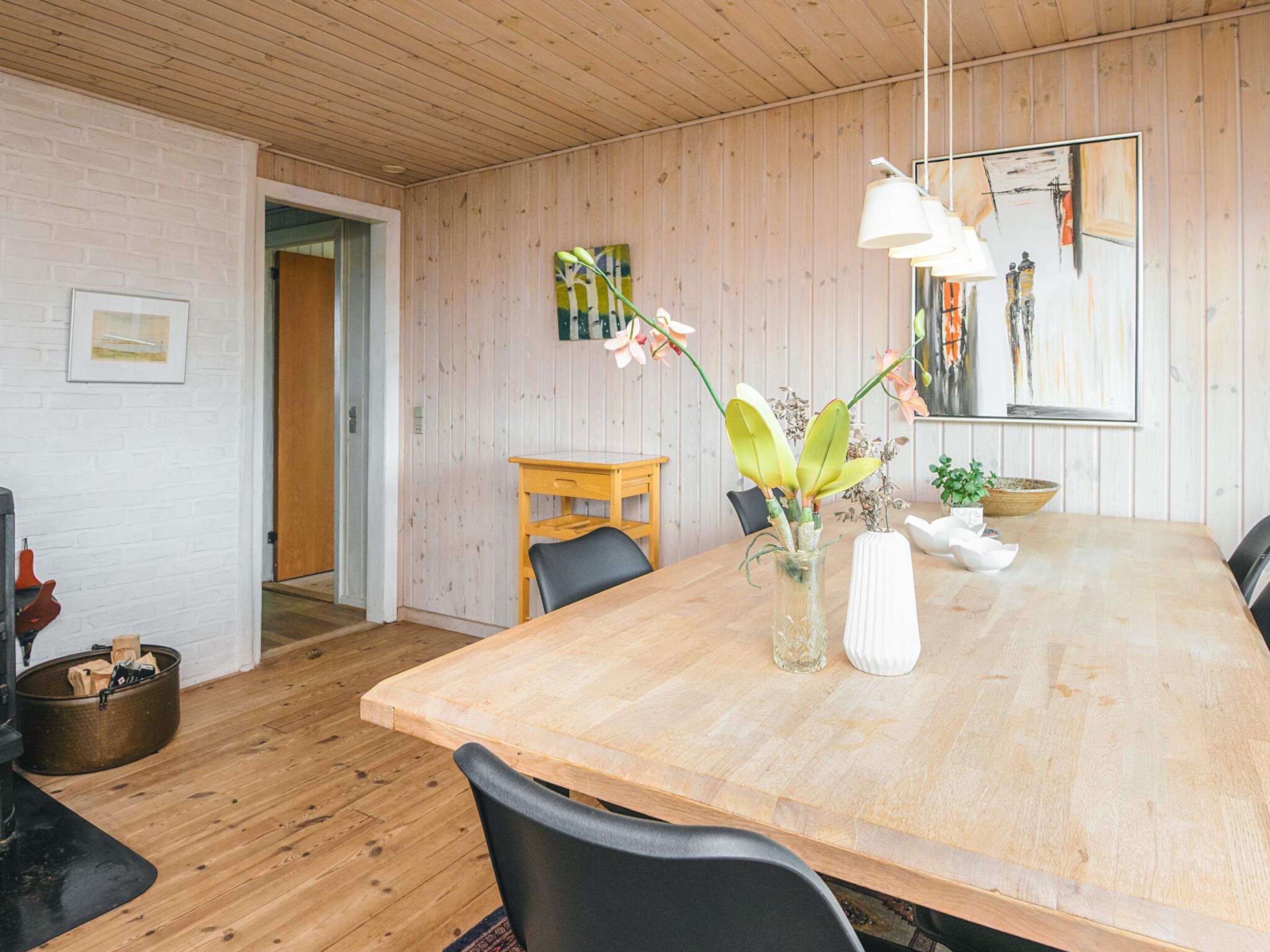 A dining area with a wooden table, chairs, a vase with flowers, and a painting on the wall.