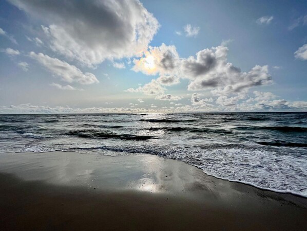 A beach with waves, a clear sky, and clouds.