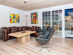 Una sala moderna con un sofá seccional de cuero marrón, una mesa de centro de madera, un sillón de cuero negro y dos cuadros abstractos en la pared.