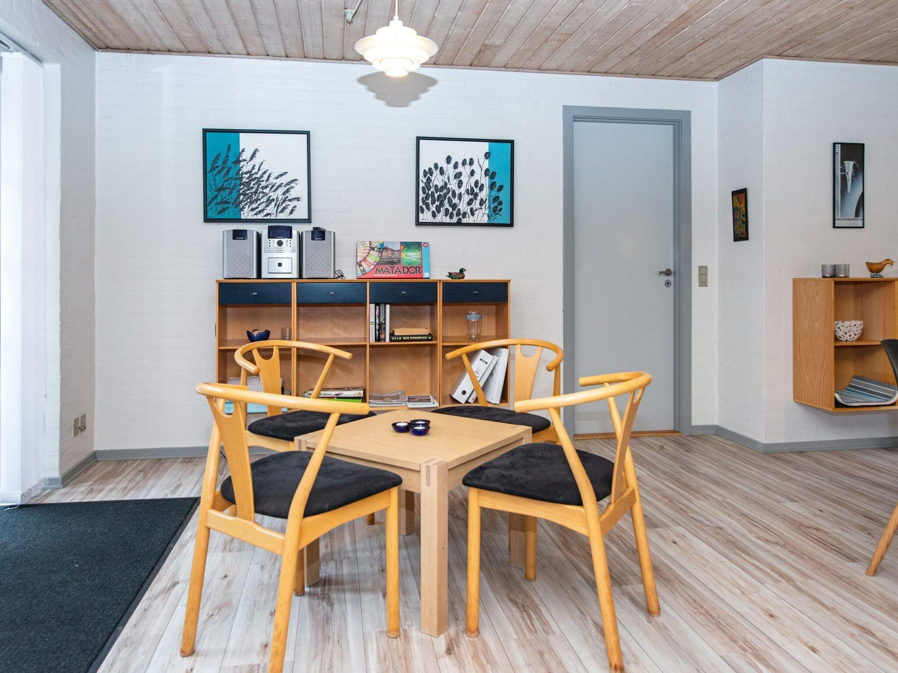 Un comedor con una mesa y sillas de madera, una estantería con libros y un juego de mesa, y una puerta al fondo.