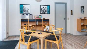 Un comedor con una mesa y sillas de madera, una estantería con libros y un juego de mesa, y una puerta al fondo.