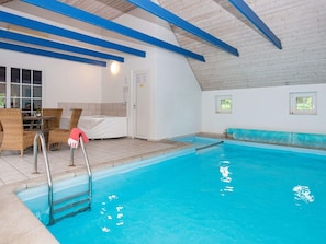 Piscina interna com teto de madeira, hidromassagem e área de estar com cadeiras de vime.