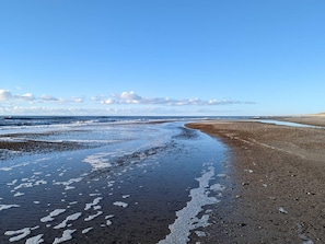 Uma praia com ondas, pedras e céu claro.