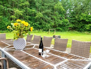 Un área de comedor al aire libre con una mesa preparada para dos, rodeada de sillas de mimbre, un jarrón de girasoles y una botella de vino.