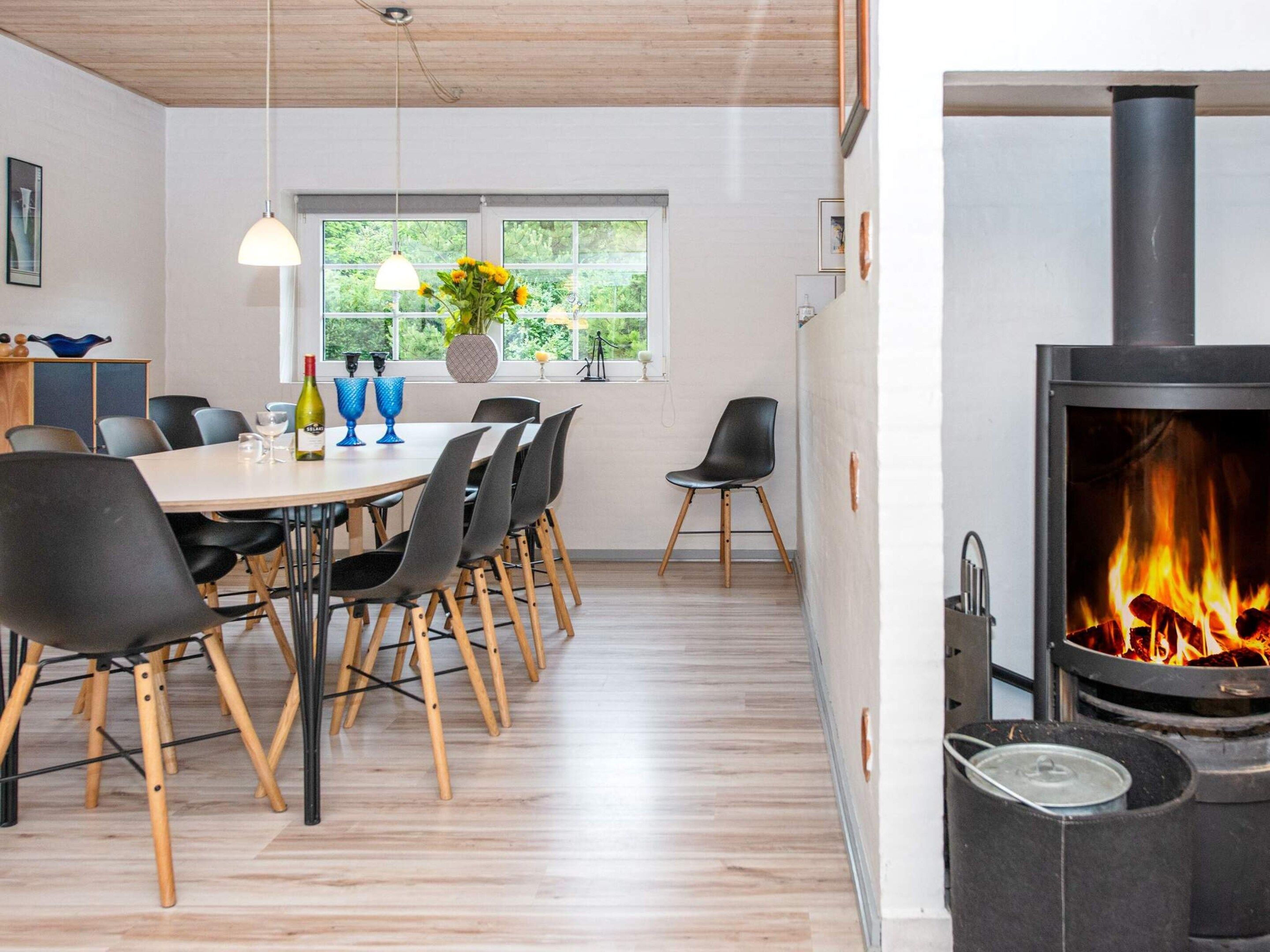 A modern dining area with a wooden table, black chairs, and a large window with a view of greenery.
