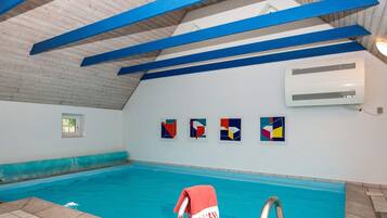 Una piscina interior con vigas azules, suelo de baldosas y una toalla roja en el escalón.