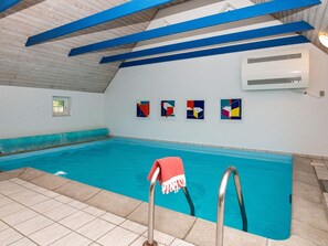 Una piscina interior con vigas azules, suelo de baldosas y una toalla roja en el escalón.