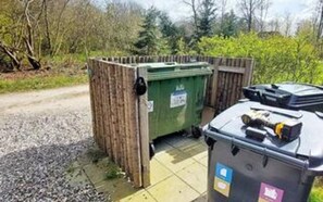 A portable toilet with a green container and a black lid, placed on a gravel path with a wooden fence in the background. - 12 Person Holiday Home in Ulfborg (Ulfborg)