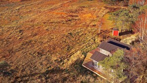 Une maison avec un toit en pente, entourée d’un paysage naturel et avec une étendue d’eau en arrière-plan.