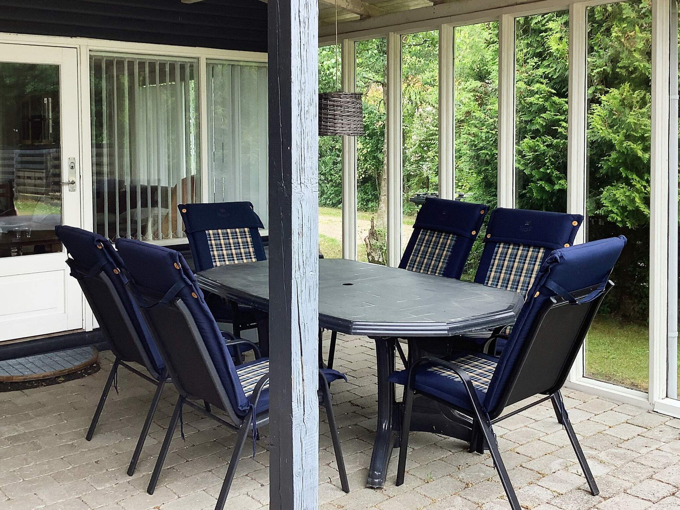 Un patio techado con mesa y sillas, un ventanal de vidrio y vistas al verdor.